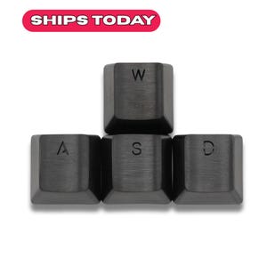 May include: A set of black keyboard keycaps with white lettering. The keys spell out "WASD" and "W". The top of the image has a red and white banner that says "SHIPS TODAY".