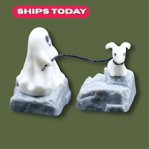 May include: A Halloween-themed figurine set. A white ghost figure holds a leash connected to a small white dog. Both figures are on grey, rocky bases. The text "SHIPS TODAY" is displayed in a pink and white banner.