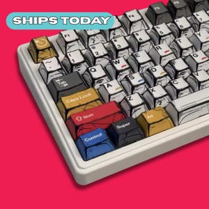 May include: A white mechanical keyboard with custom keycaps. The keycaps have a comic book style design with black outlines and various colors. The keyboard includes the text "SHIPS TODAY" in a blue and white banner.