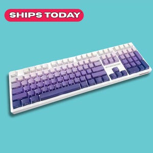 May include: A white mechanical keyboard with purple gradient keycaps. The keyboard has a white frame and a standard layout. The keys transition from white to shades of purple. The text "SHIPS TODAY" is in a red banner.