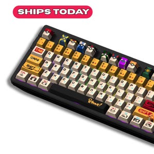 Könnte beinhalten: Schwarze mechanische Tastatur mit individuellen Tastenkappen mit farbenfrohem Design. Die Tastenkappen haben japanische Schriftzeichen und verschiedene grafische Designs. Die Tastatur hat den Text "Pokemon" auf der Vorderseite. Der Text "SHIPS TODAY" steht in einem roten Banner oben.