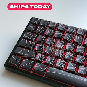 Könnte beinhalten: Eine schwarze mechanische Tastatur mit Tastenkappen mit einem weißen Netzdesign. Die Tastatur hat eine rote Hintergrundbeleuchtung und den Text "SHIPS TODAY" in einem rosa-weißen Banner.