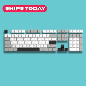 Könnte beinhalten: Zerlegtes mechanisches Keyboard mit weißen, grauen und schwarzen Tastenkappen. Das Layout ist sichtbar, mit alphanumerischen Tasten, Funktionstasten und einem Nummernblock. Der Hintergrund ist türkis.