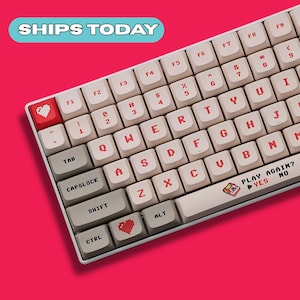 May include: A white mechanical keyboard with red lettering and accents. The keyboard has a red heart key and the text "PLAY AGAIN? YES NO". The background is a solid pink color.