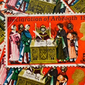 May include: A vintage postage stamp featuring a historical scene with the text "Declaration of Arbroath 1320". The stamp is red, orange, and gold with a depiction of people in medieval clothing. The stamp has a 5d denomination.
