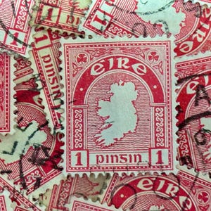 May include: A close-up of a collection of vintage Irish postage stamps featuring the outline of Ireland and the text "EIRE" and "1 pinsin 1". The stamps are red and white with a decorative border.