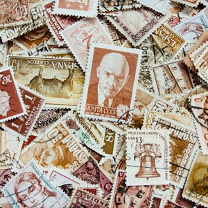 Op de afbeelding: Een verzameling vintage postzegels, met verschillende ontwerpen en kleuren. Postzegels tonen portretten, historische figuren en bezienswaardigheden. De postzegels zijn in een verspreid patroon gerangschikt, wat hun diverse oorsprong laat zien.