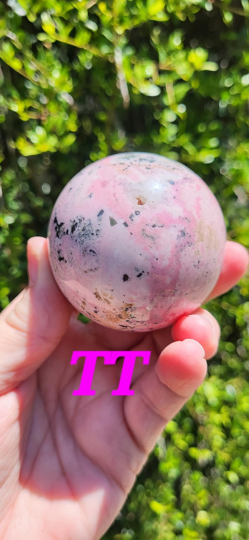 K&ouml;nnte beinhalten: Eine rosa-graue Kugel mit einem gesprenkelten Muster wird in einer Hand gehalten. Die Kugel hat eine polierte Oberfl&auml;che und scheint ein Edelstein oder ein dekoratives Objekt zu sein. Die Buchstaben "TT" sind auf dem Bild &uuml;berlagert.