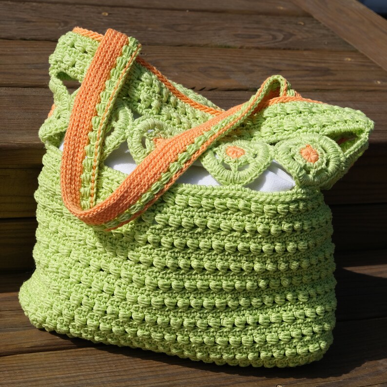 Pu&ograve; includere: Una borsa a mano in crochet verde con una tracolla in crochet arancione brillante. La borsa ha un design a pizzo ed &egrave; perfetta per portare gli oggetti essenziali di tutti i giorni.