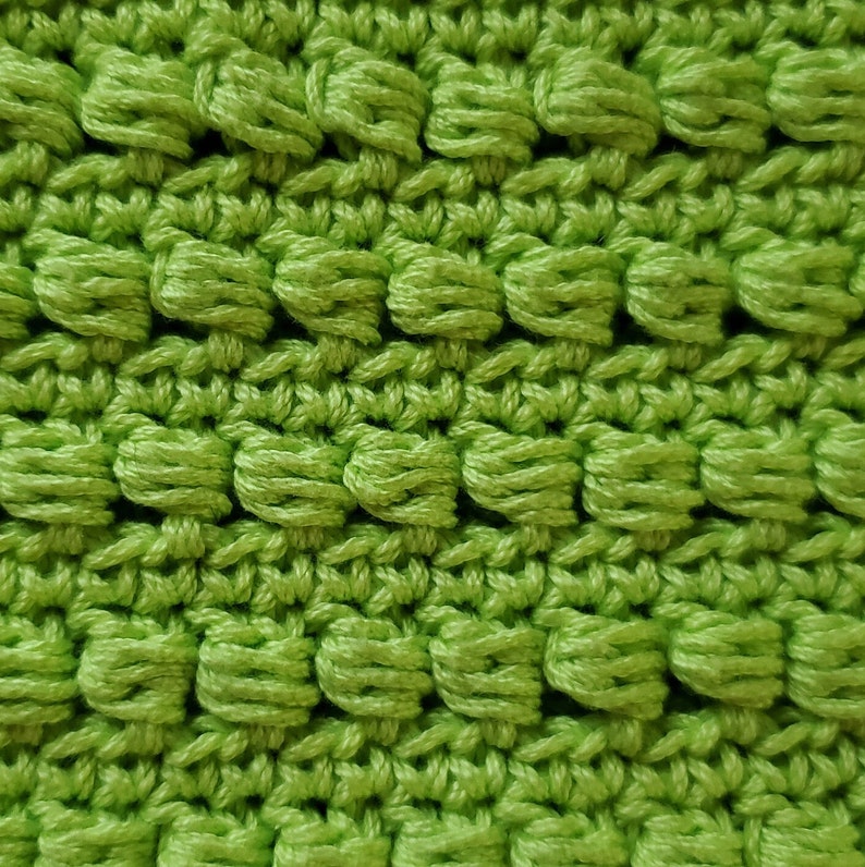 Pu&ograve; includere: Primo piano di un tessuto lavorato a uncinetto verde con una superficie testurizzata e irregolare.