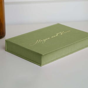 Peut inclure: Une boîte recouverte de tissu vert avec l'inscription "Megan et Kevin" en lettres dorées.