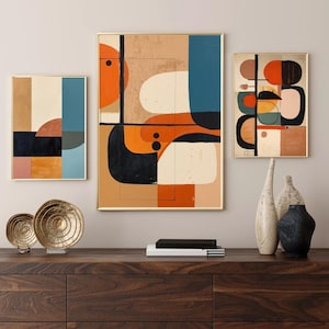 May include: Three framed abstract art prints with gold frames. The artwork features geometric shapes in orange, black, blue, and beige. The prints are displayed above a dark wooden cabinet with decorative items.