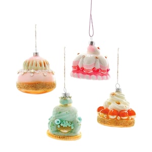 May include: Four glass Christmas ornaments shaped like different pastries. The ornaments are decorated with frosting, sprinkles, and beads. The ornaments are hanging from strings.