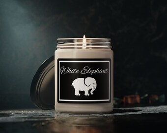 Könnte beinhalten: Eine weiße Kerze in einem Glasgefäß mit einem schwarzen Etikett, auf dem "White Elephant" steht und eine weiße Silhouette eines Elefanten abgebildet ist. Die Kerze ist angezündet und die Flamme ist sichtbar.