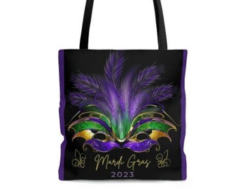 May include: Black tote bag with a purple, green, and gold Mardi Gras mask design. The mask has feathers and the text "Mardi Gras 2023" is below it.