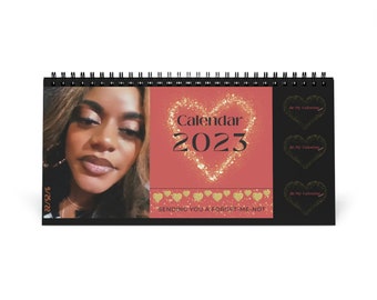 May include: A black calendar with a pink background and gold glitter hearts. The calendar features a photo of a woman and the text "Calendar 2023" and "Sending you a forget-me-not".