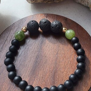 May include: Black beaded bracelet with green and gold accents. The bracelet is made with lava rock and agate beads.