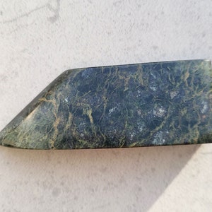 Pode incluir: Uma pedra de cor verde escura, de forma irregular, com um padrão de veios verde claro e dourados.