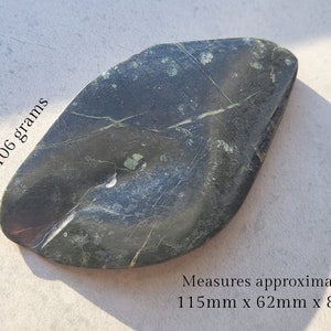 May include: A dark green, irregularly shaped stone with white and black veins. It weighs 106 grams and measures approximately 115mm x 62mm x 8mm.