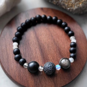May include: Black beaded bracelet with white beads, a black lava bead, a silver obsidian bead, and a clear crystal bead.