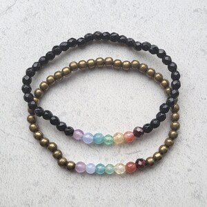 May include: Two bracelets, one black and one gold, with a rainbow of colored beads in between.