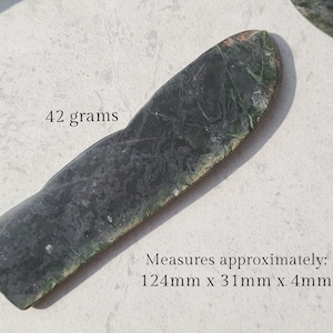 Könnte beinhalten: Ein dunkelgrüner, schwarzer und weißer Stein mit den Maßen 124 mm x 31 mm x 4 mm und einem Gewicht von 42 Gramm. Der Stein hat eine glatte, polierte Oberfläche und ein einzigartiges, natürliches Muster.