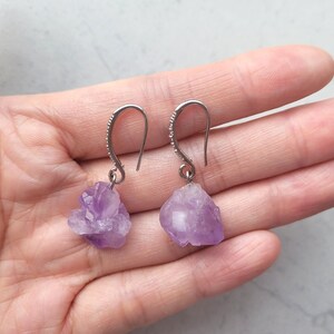 May include: A pair of silver earrings with purple amethyst crystal drops. The crystals are irregularly shaped and have a natural, raw look.