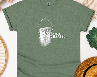 May include: A green t-shirt with a white image of Saint Charbel, a Lebanese Maronite Catholic priest, on the front. The text "SAINT CHARBEL" is printed below the image.