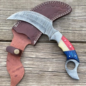 May include: A curved, stainless steel knife with a Damascus pattern blade and a red, white, and blue handle. The knife comes with a brown leather sheath.