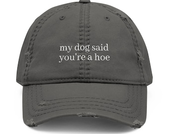 May include: Distressed gray baseball cap with the text "my dog said you're a hoe" in white. The cap has a curved brim and a worn, vintage look, with distressed details around the edges.
