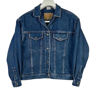 May include: A medium-wash blue denim jacket with a classic design. Features include a collared neckline, button-down front, two chest pockets, and buttoned cuffs. The jacket has a vintage look and feel, perfect for casual wear.