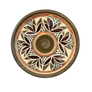 May include: A round, ceramic serving dish with a central dip bowl. The dish features a floral pattern in brown, cream, and green, with a dark brown rim. The dip bowl is a darker shade of green.