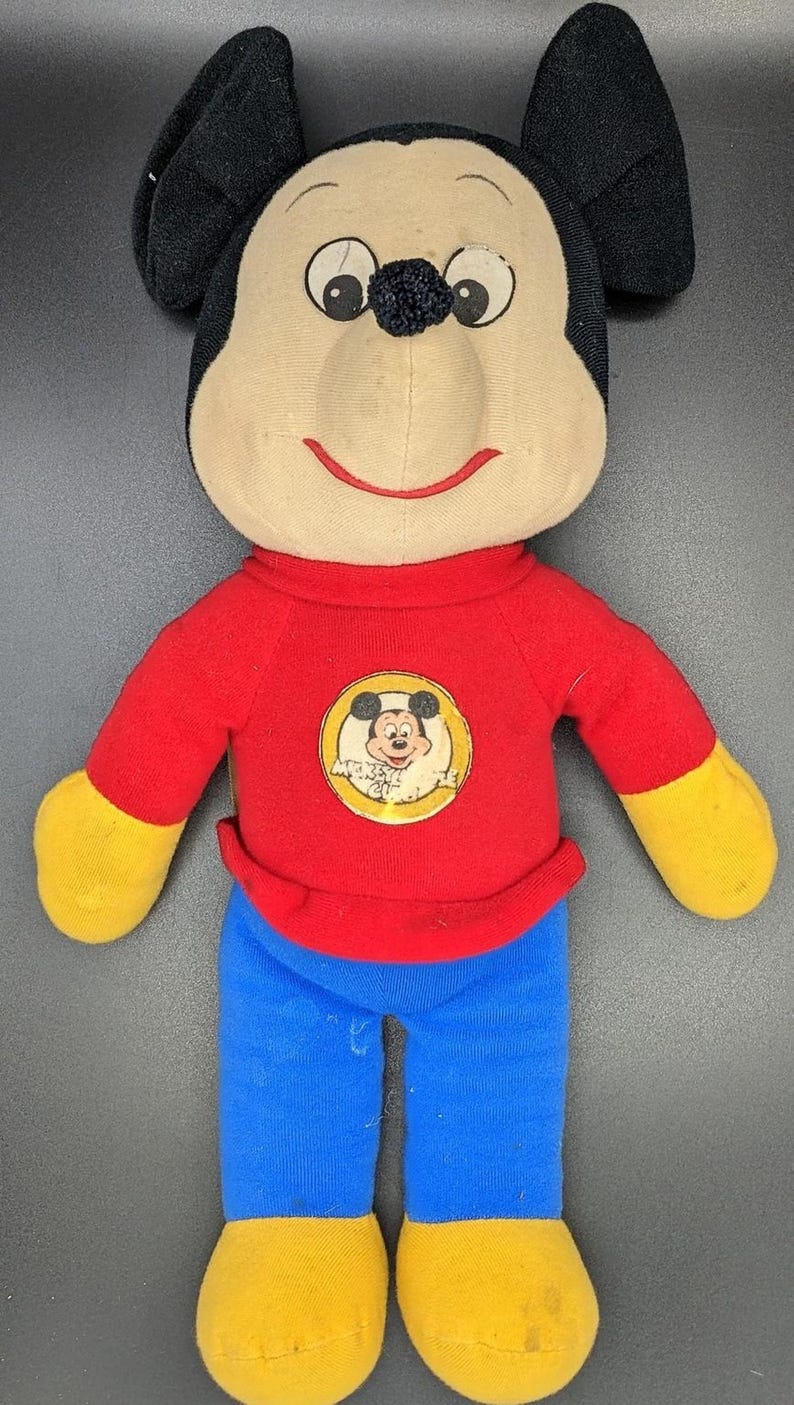 A plush toy of Mickey Mouse wearing a red shirt and blue pants.