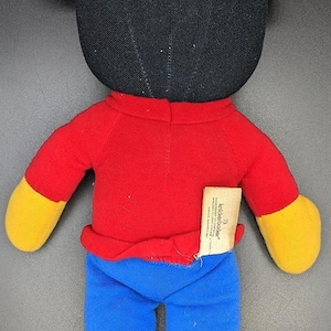 A plush toy of Mickey Mouse wearing a red shirt and blue pants.