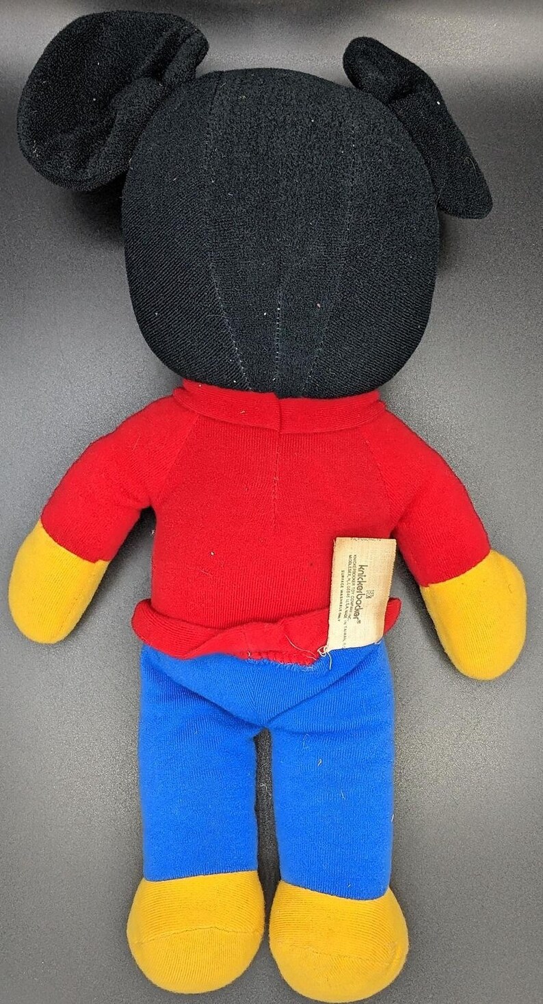 A plush toy of Mickey Mouse wearing a red shirt and blue pants.