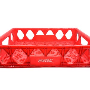 Peut inclure: Une caisse rectangulaire en plastique rouge Coca-Cola avec une base à motif de grille et des parois latérales ouvertes dotées de découpes en forme de losange. Le panneau avant affiche le logo blanc Coca-Cola. Structure de rangement.