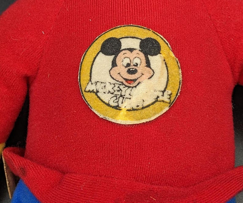 A red sweater with a circular patch featuring a cartoon character, likely Mickey Mouse, on it.