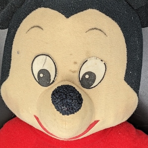 A close-up of a stuffed toy resembling Mickey Mouse, with a red shirt and a black nose.