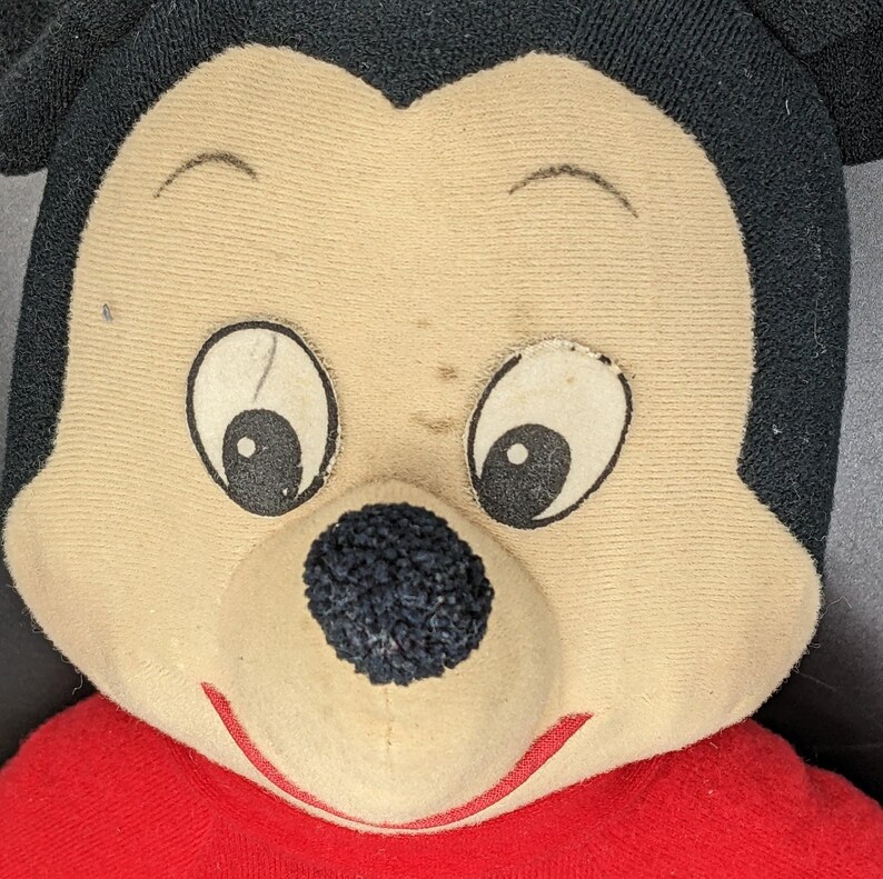 A close-up of a stuffed toy resembling Mickey Mouse, with a red shirt and a black nose.