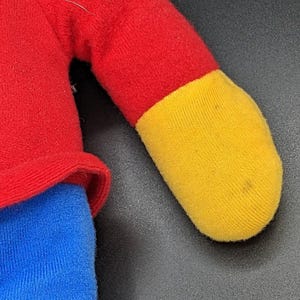 A close-up view of a plush toy with a red and yellow color scheme, featuring a red shirt and a yellow sock.