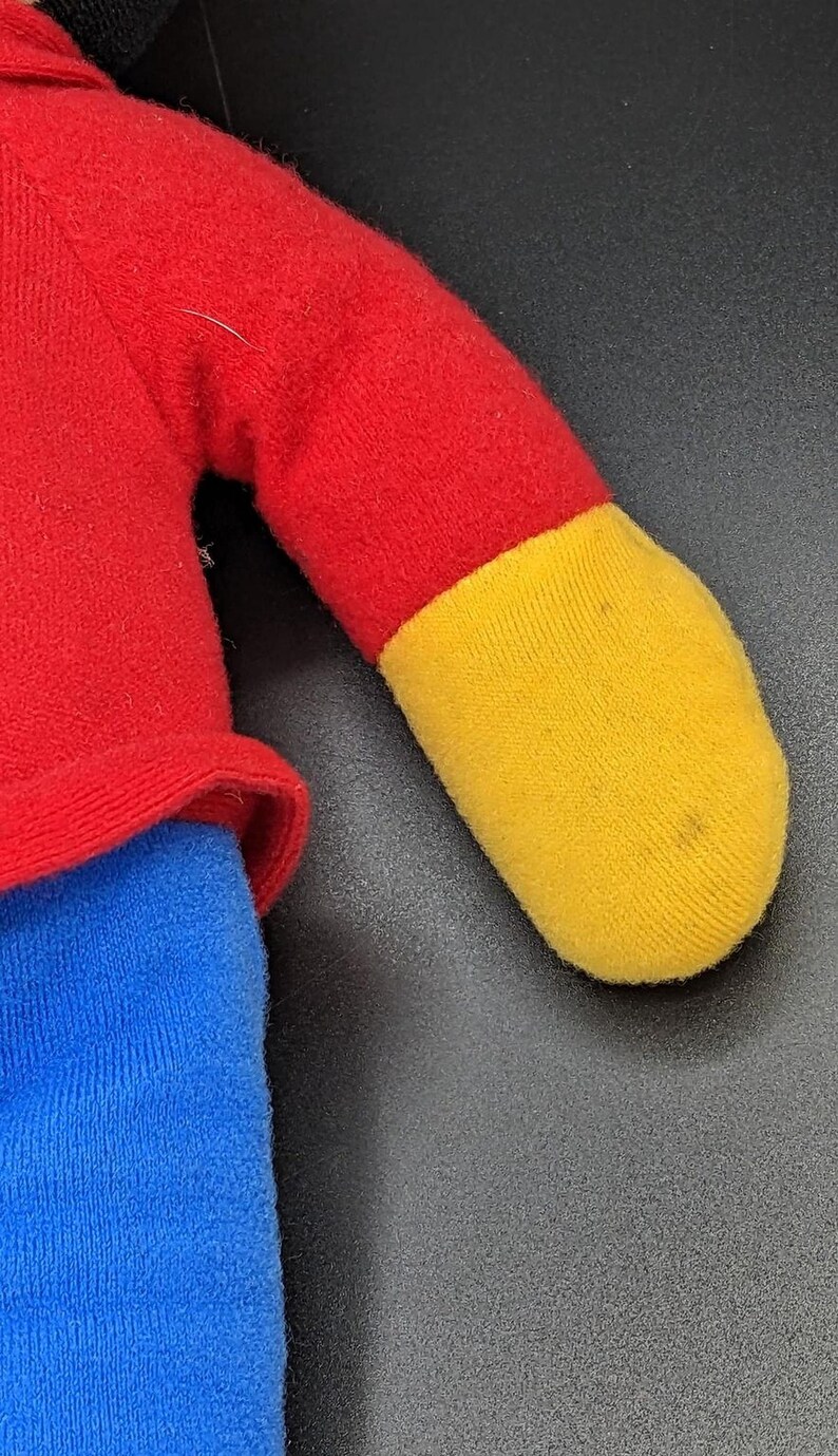 A close-up view of a plush toy with a red and yellow color scheme, featuring a red shirt and a yellow sock.