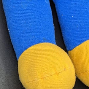 A close-up view of a blue and yellow toy, likely a stuffed animal, with a yellow sock and a blue sock visible.