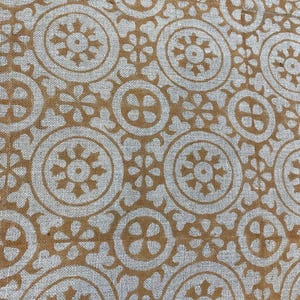 May include: Close-up of a fabric with a repeating pattern of tan circles and floral shapes on a light gray background. The design has a vintage or bohemian aesthetic, suitable for textiles or home decor.