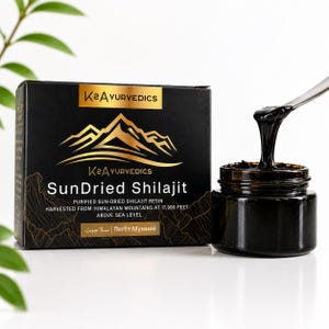 May include: A black box labeled K2Ayurvedics SunDried Shilajit with a gold mountain graphic, next to a small dark glass jar containing a thick black resin. A metal spatula lifts a portion of the viscous substance from the open jar container.