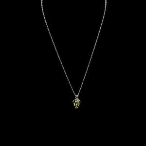 Puede incluir: Un delicado collar de plata con un peque&ntilde;o colgante en forma de jaula que contiene una piedra preciosa verde claro. El colgante cuelga de una fina cadena sobre un fondo negro, resaltando el intrincado dise&ntilde;o y el contraste de color de la joya.