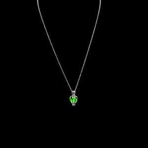 Puede incluir: Un collar plateado con un peque&ntilde;o colgante en forma de jaula que contiene una piedra verde brillante. El colgante cuelga de una fina cadena sobre un fondo negro. El collar es una joya sencilla y elegante.