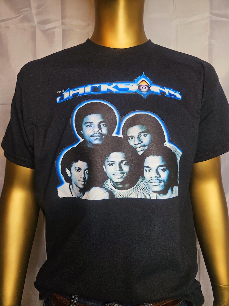 May include: Black t-shirt with a blue and white graphic of the Jackson 5. The graphic features a photo of the band members and the text "The Jacksons" in a blue and white font.