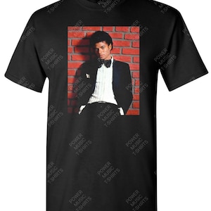 May include: Black t-shirt with a graphic print of Michael Jackson in a tuxedo, standing in front of a brick wall. The text "POWER MUSIC T-SHIRTS" is repeated throughout the image.