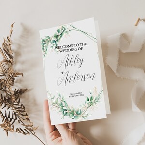 Pode incluir: Um convite de casamento branco com uma moldura geométrica dourada e um design floral em aquarela verde. O texto diz "Bem-vindos ao casamento de Ashley + Anderson, 20 de maio de 20xx, Bath, Inglaterra."