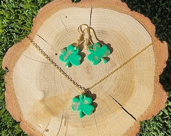 May include: A gold chain necklace and matching earrings with green shamrock charms. The charms have a glittery gold finish.